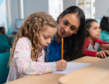 A tutor working with a young girl who is writing using a pencil.