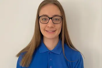 This image shows a tutor who is young woman in a blue Explore Learning polo shirt standing in front of a plain white wall.