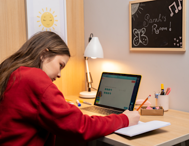 A teenage child works on a laptop at a desk