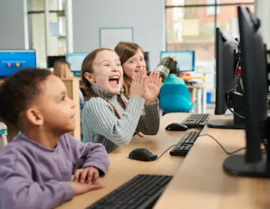 Three children sit at a desk learning on computers.