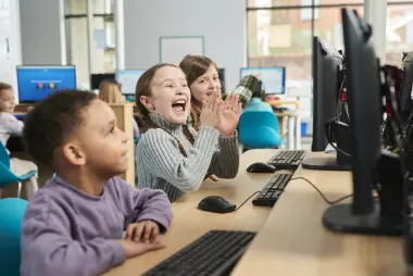 Three children sit at a desk learning on computers.