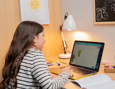 A boy sits at a desk working on a laptop.