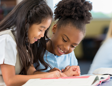 Two girls sit together reading a book.