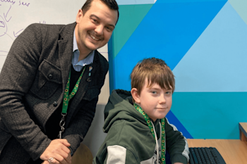 Centre Director, Sean, with an Explore Learning member at a computer, both are wearing a sunflower lanyard, which is a symbol for people to showcase that they have a hidden disability. 