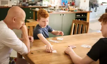 2 boys playing cards with their dad on the dining table