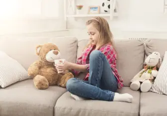 beautiful little girl on a sofa treating her teddy bear with tea