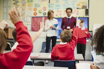 Children in school with teachers putting their hands up