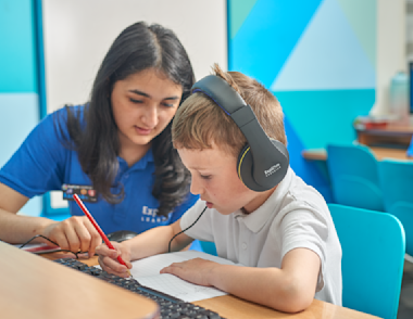 An Explore Learning tutor sat at a desk with a child writing in a workbook.