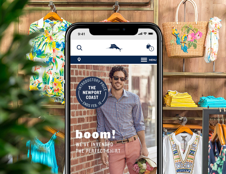 Tommy Bahama website shown on mobile device with Hawaiian shirts, bag and apparel in the background