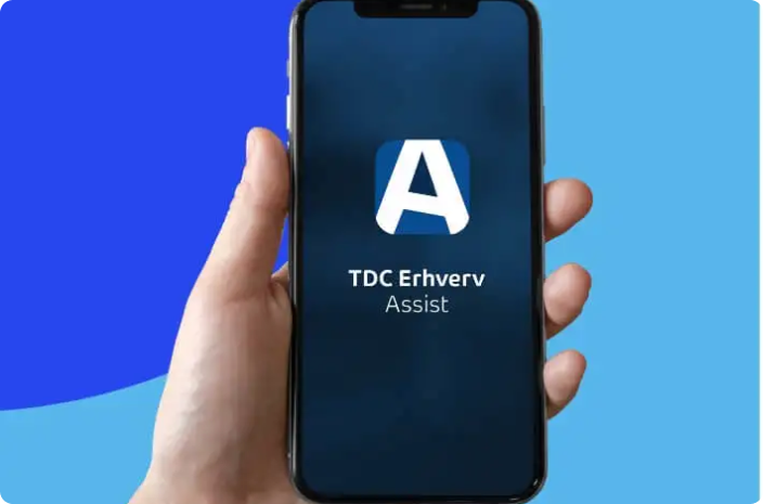 En hånd holder en mobiltelefon med TDC Erhverv Assist App logo