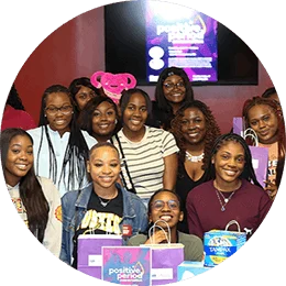 A group of seventeen young black college women gather and smile in front a table displaying Tampax period products and packaging.