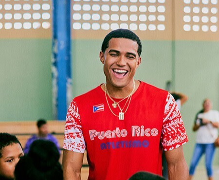 A young Hispanic man in a red shirt smiles as he engages with children at a school.