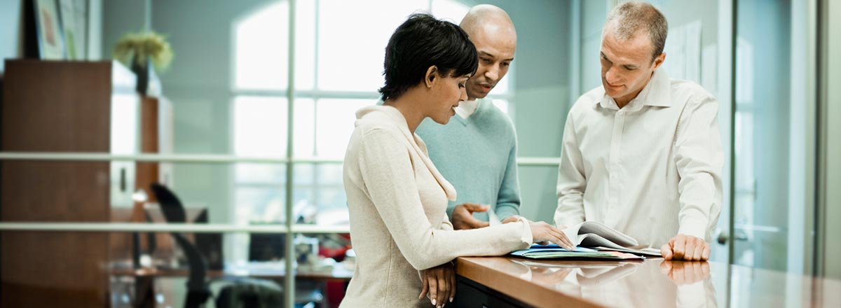 3 coworkers standing at a table looking at a printed report