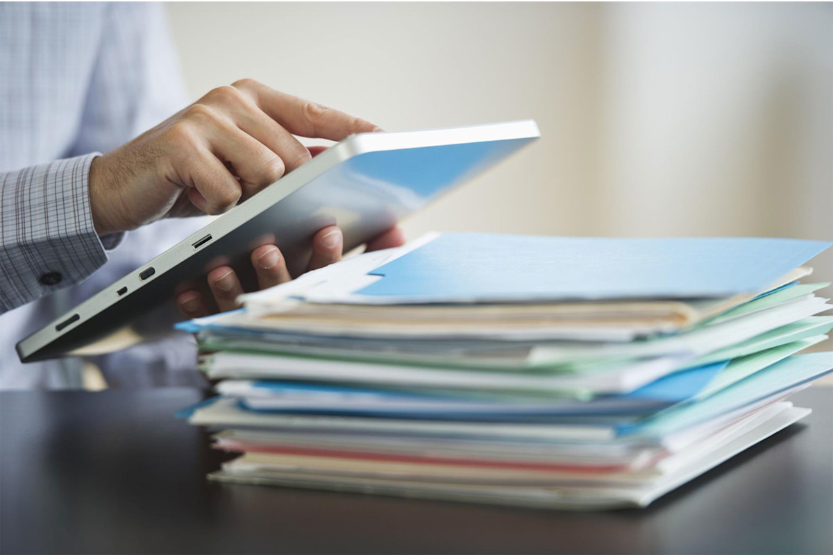 Man holding tablet with stack of files