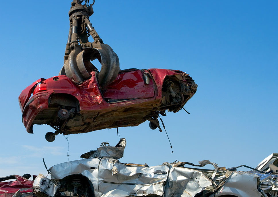 A scrap car being picked up by a claw grabber