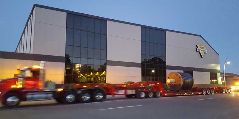Large flatbed truck driving past Bowe Machine Company building