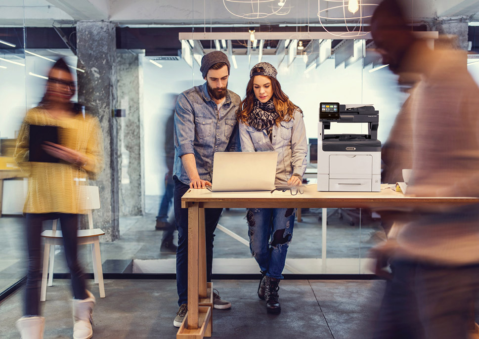 Man and woman in a busy modern office with a Xerox VersaLink C405 MFP
