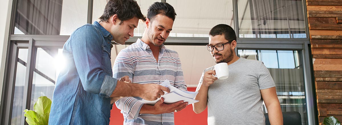 Three co-workers standing together looking at printed documents