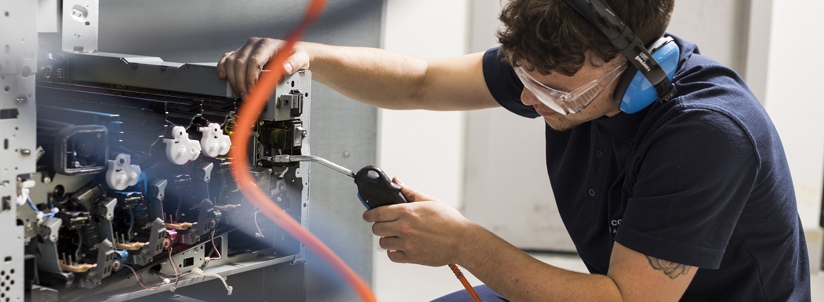 Man working on a printer with ear muffs and glasses