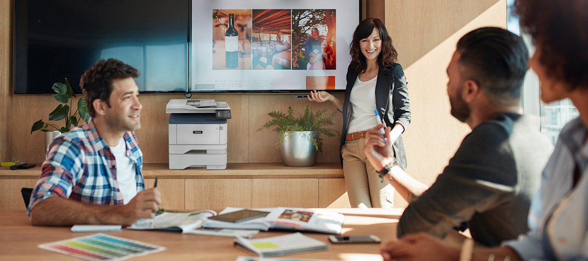 Business meeting with a Xerox MFP in the background and printed charts on the conference table