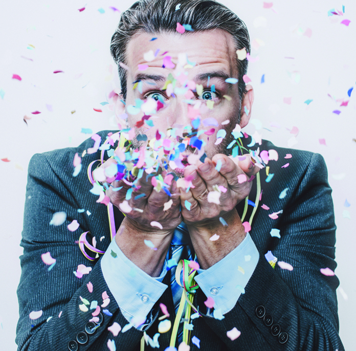 Man in a business suit blowing confetti into the air