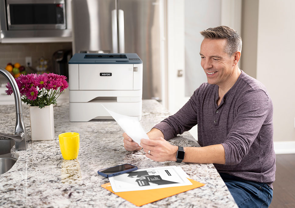 Man sitting at kitchen counter looking at paperwork with Xerox B310 Printer behind him