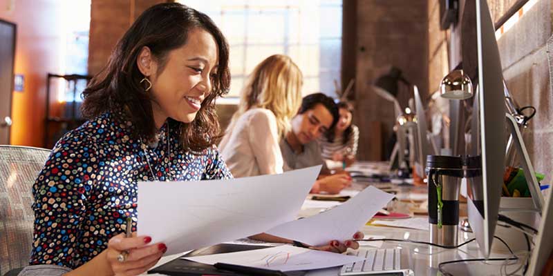 A row of employees at a long desk. The closest woman is sorting papers.