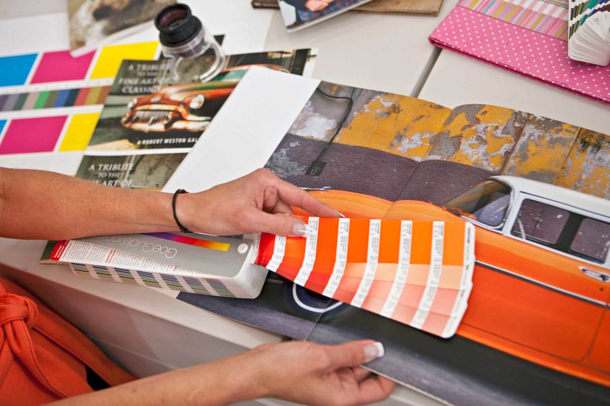 Print shop employee comparing swatches in different shades of orange to a print sample with an orange car