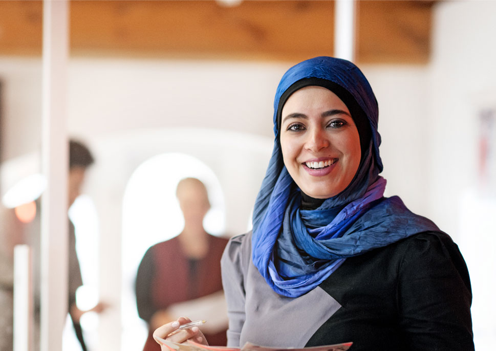 Smiling woman in a hijab holding a stack of papers