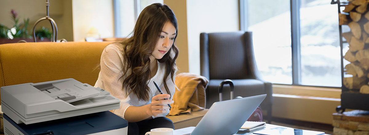 A woman with a laptop using a Xerox C235 MFP in her home office