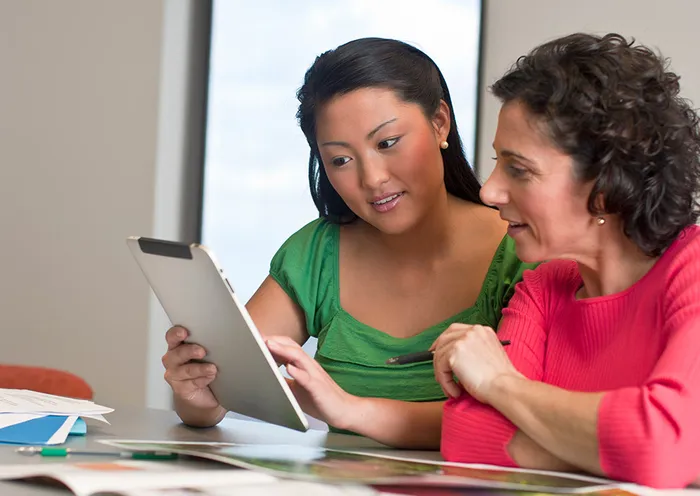 Two women looking at a tablet and print samples