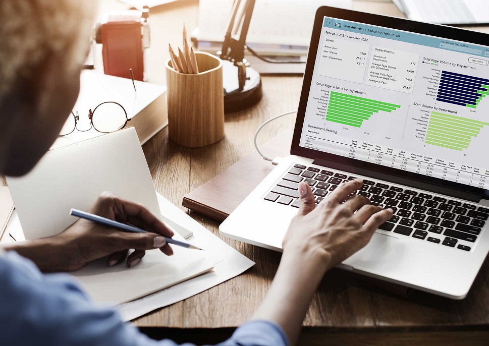 Person with a pencil in their hand, analyzing graphs on a laptop screen