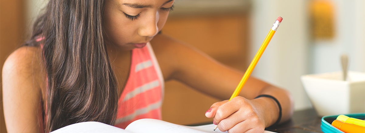 Young girl writing in a workbook with a pencil