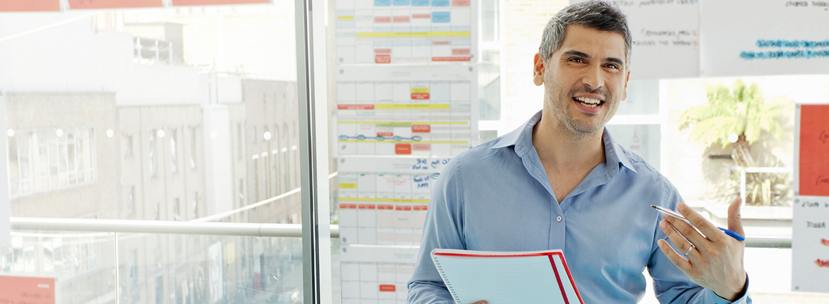 A man giving a presentation in a meeting room with charts behind him