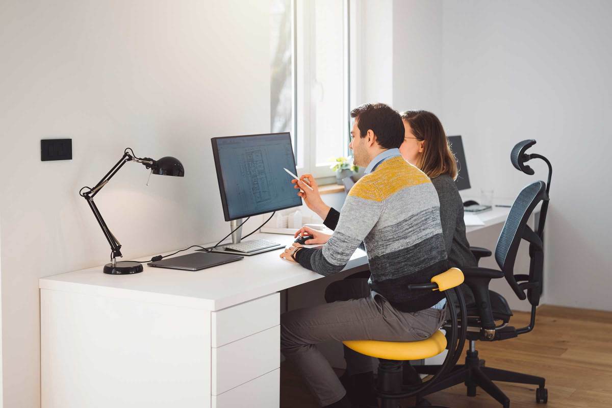 Two people sitting together at a desk looking at a monitor, with a desk lap beside them