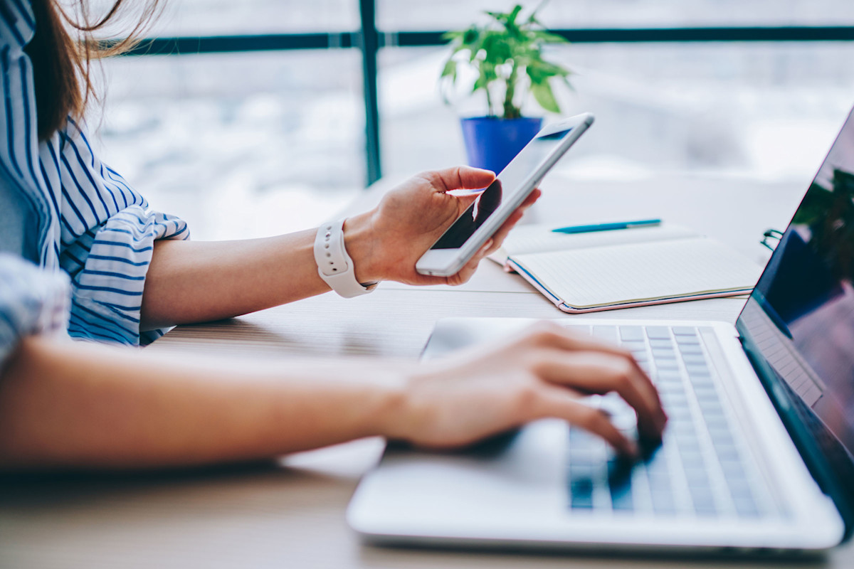Woman working on laptop and looking at smartphone