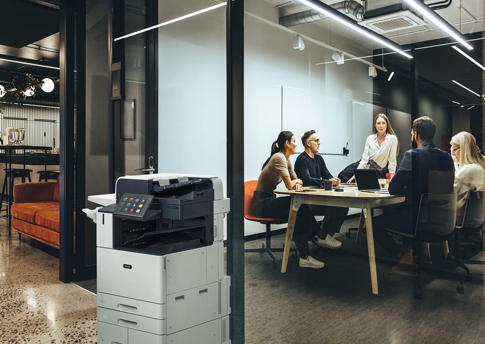 AltaLink Printer in front of conference room with people in it.