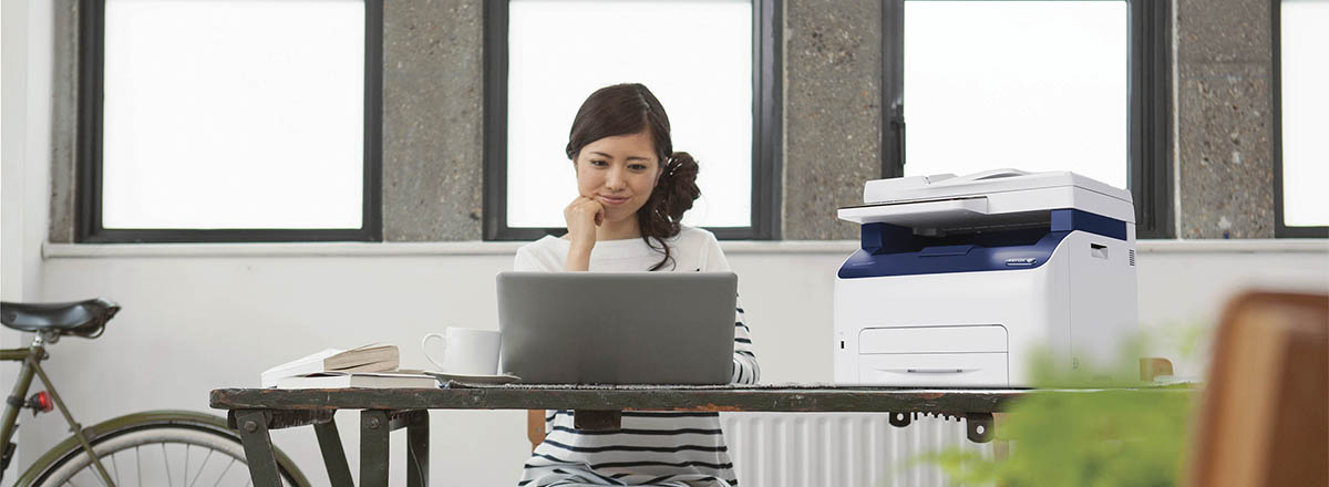 Woman using a laptop in an office with a Xerox MFP beside her