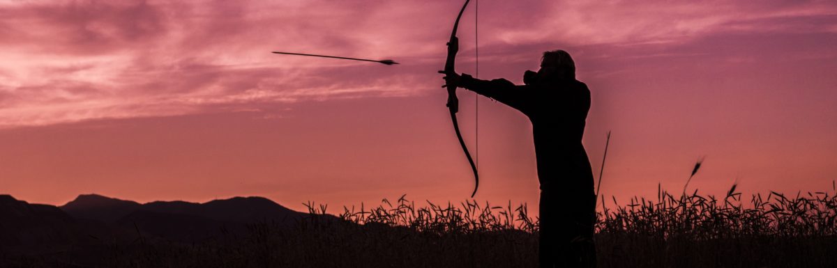 A man shooting a bow and arrow at sunset