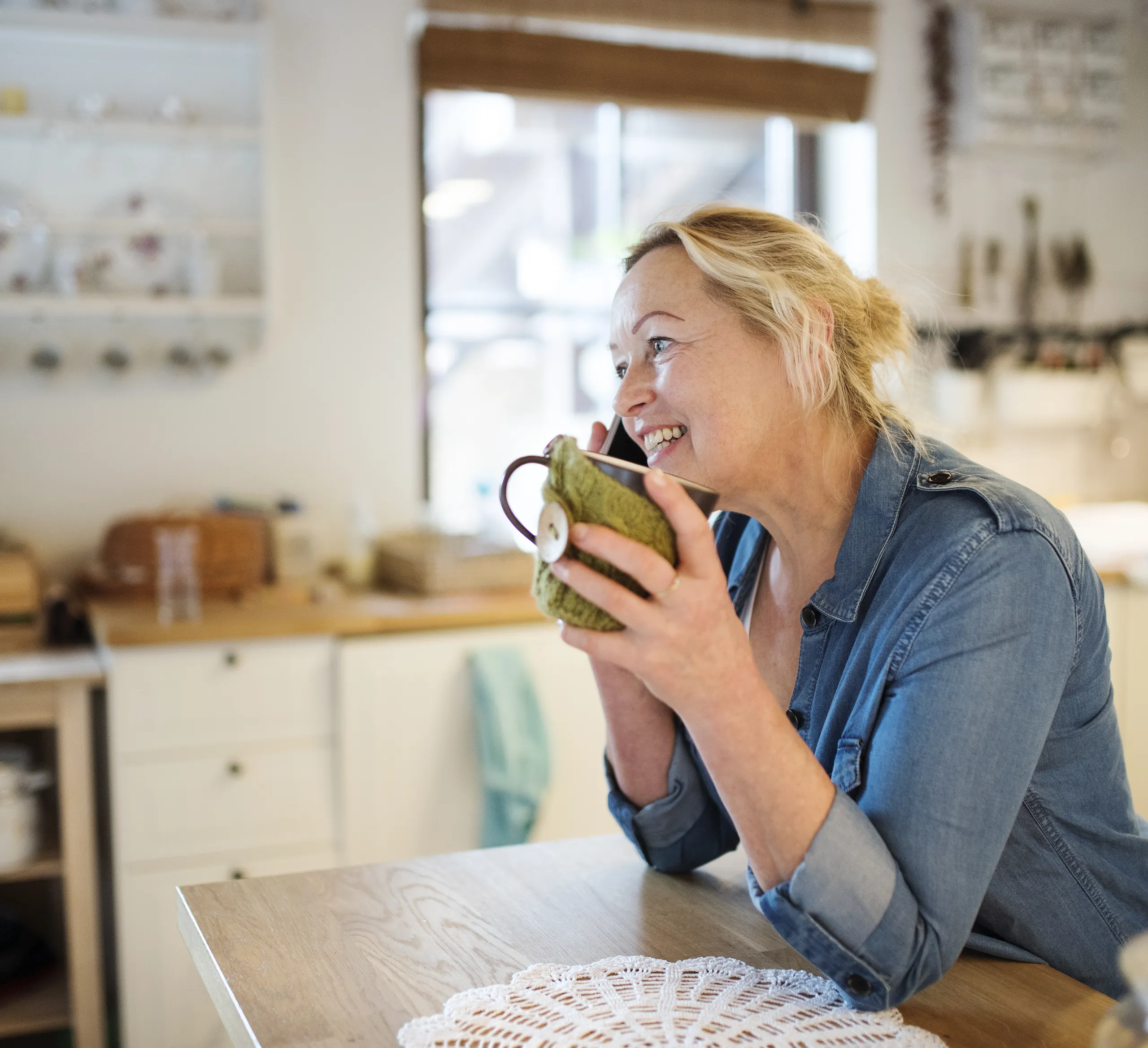 woman on a phonecall, drinking tea in the kitchen