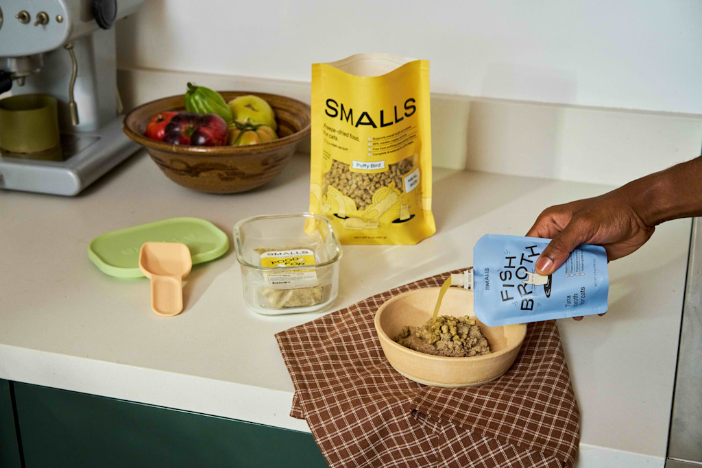 A hand pours Fish Broth on a bowl of Smalls fresh food and freeze-dried puffs.