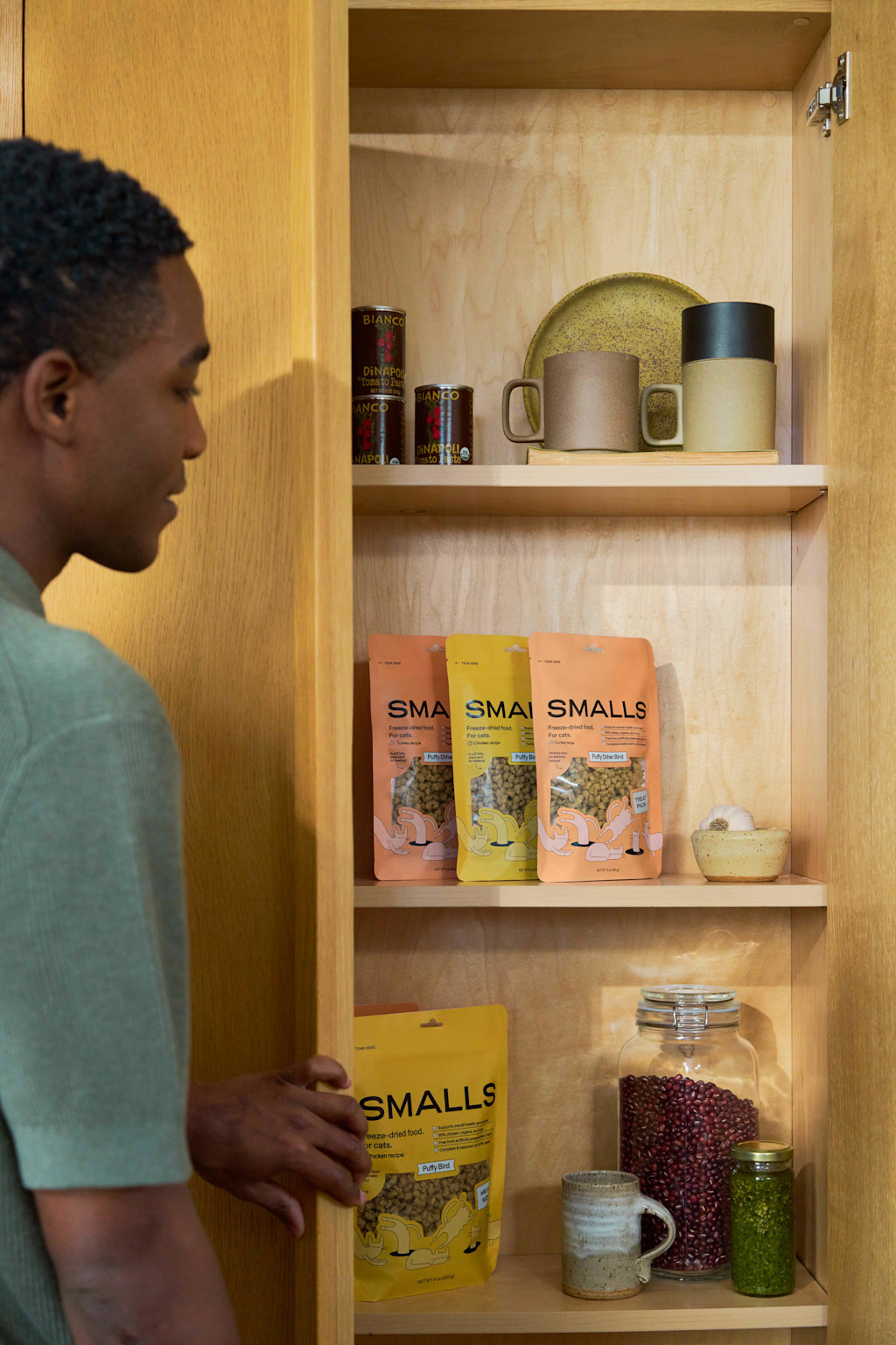 vertical image of a man opening a kitchen cabinet where packets of freeze-dried food sits