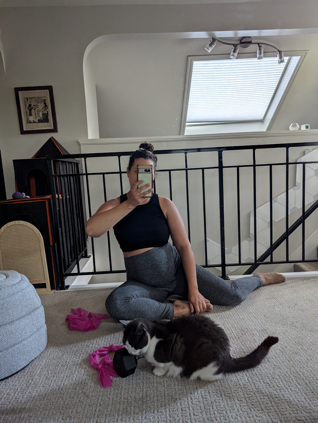 Janelle sits on the floor for a mirror selfie while working out. Lyra is keeping watch over her weights.