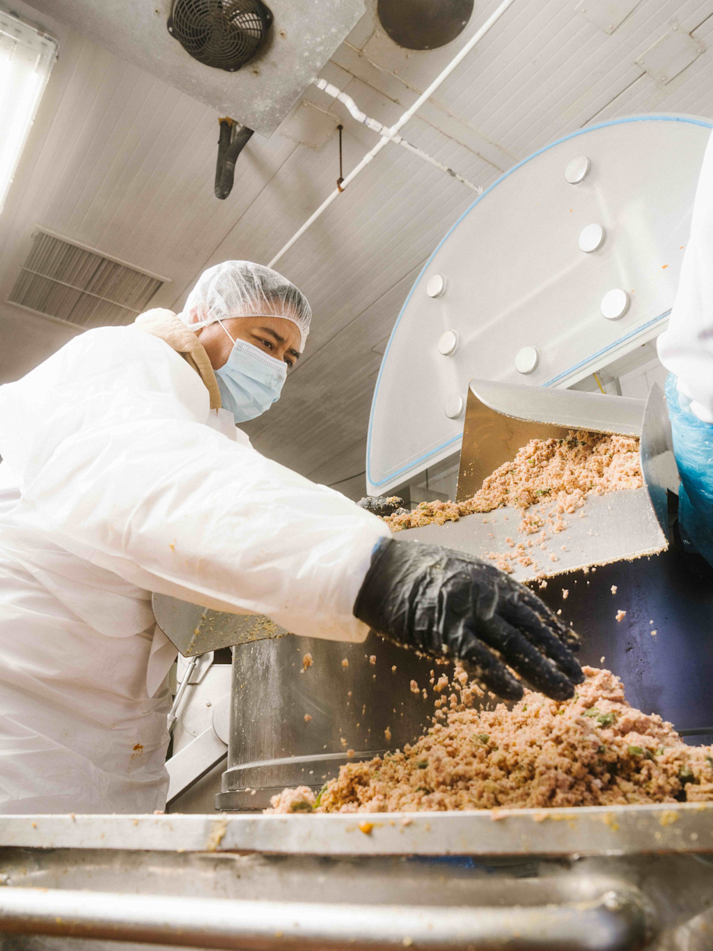 Man in attire safe for food handling, guides Smalls fresh food from one machine to another.