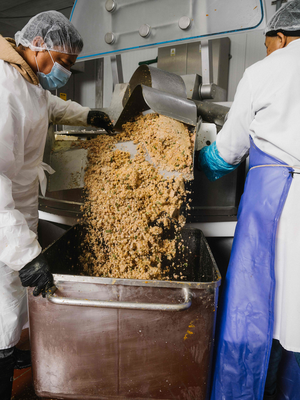 Two men in attire safe for food handling guide large amounts of fresh food