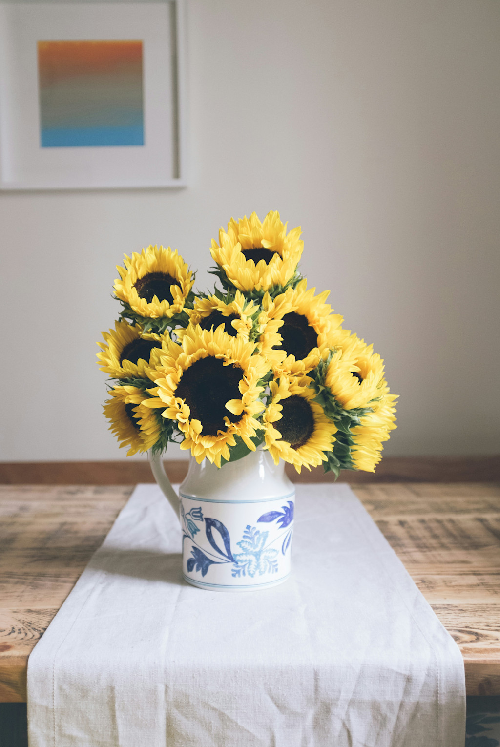 Vase of yellow sunflowers on a table runner atop a wooden table.