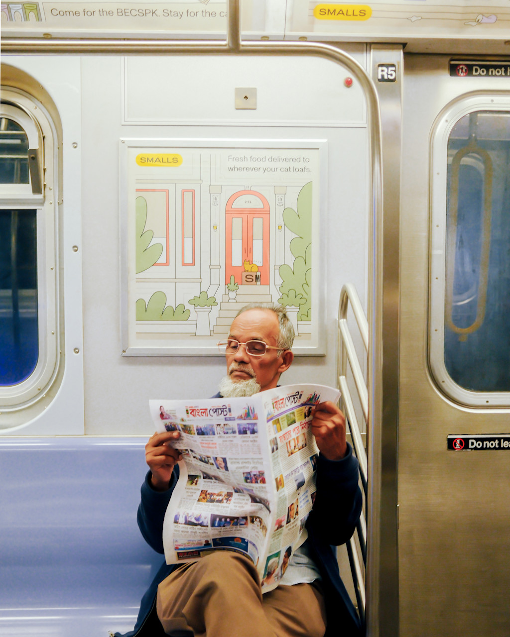 Man with gray hair sits on the the subway bench reading a newspaper