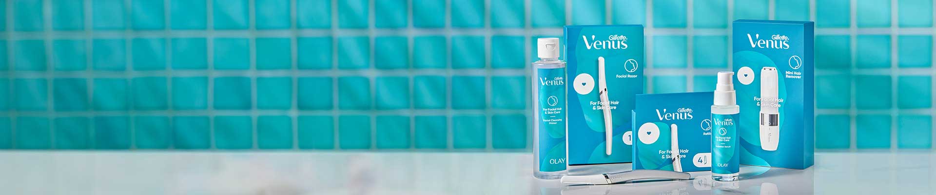 Línea de productos de cuidado facial y para la piel de Gillette Venus en un baño azul: Primer, Maquinilla de afeitar, Recambios, Suero y Recortadora.