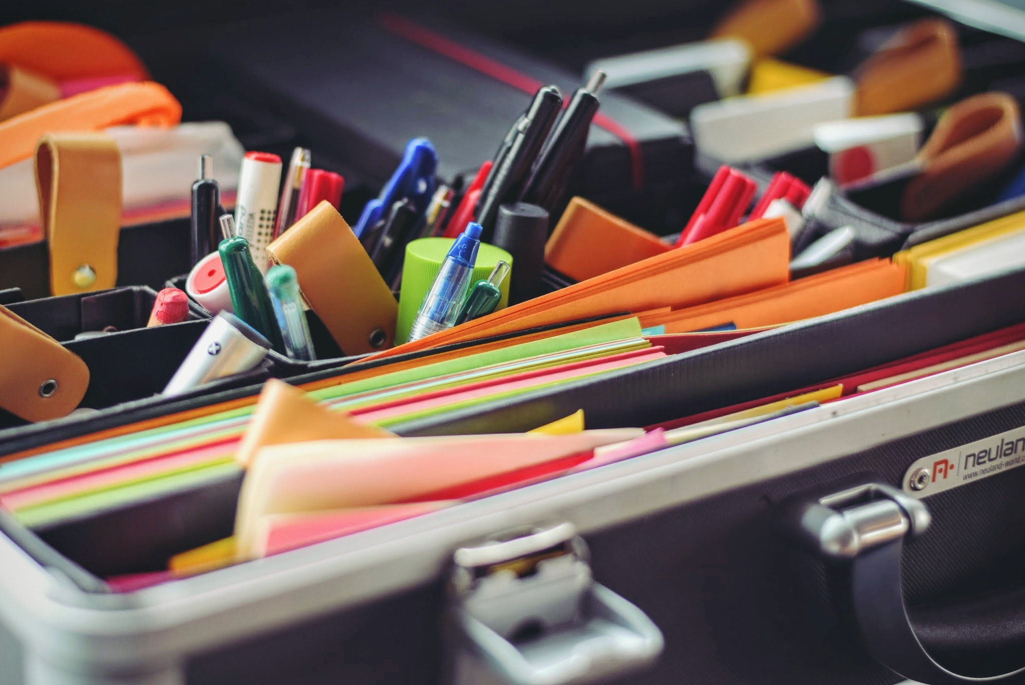 Photo of various office supplies, pens, coloured paper, scissors in green, black and orange