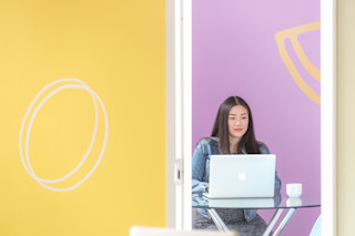 Woman sitting in front of yellow and pink walls with laptop